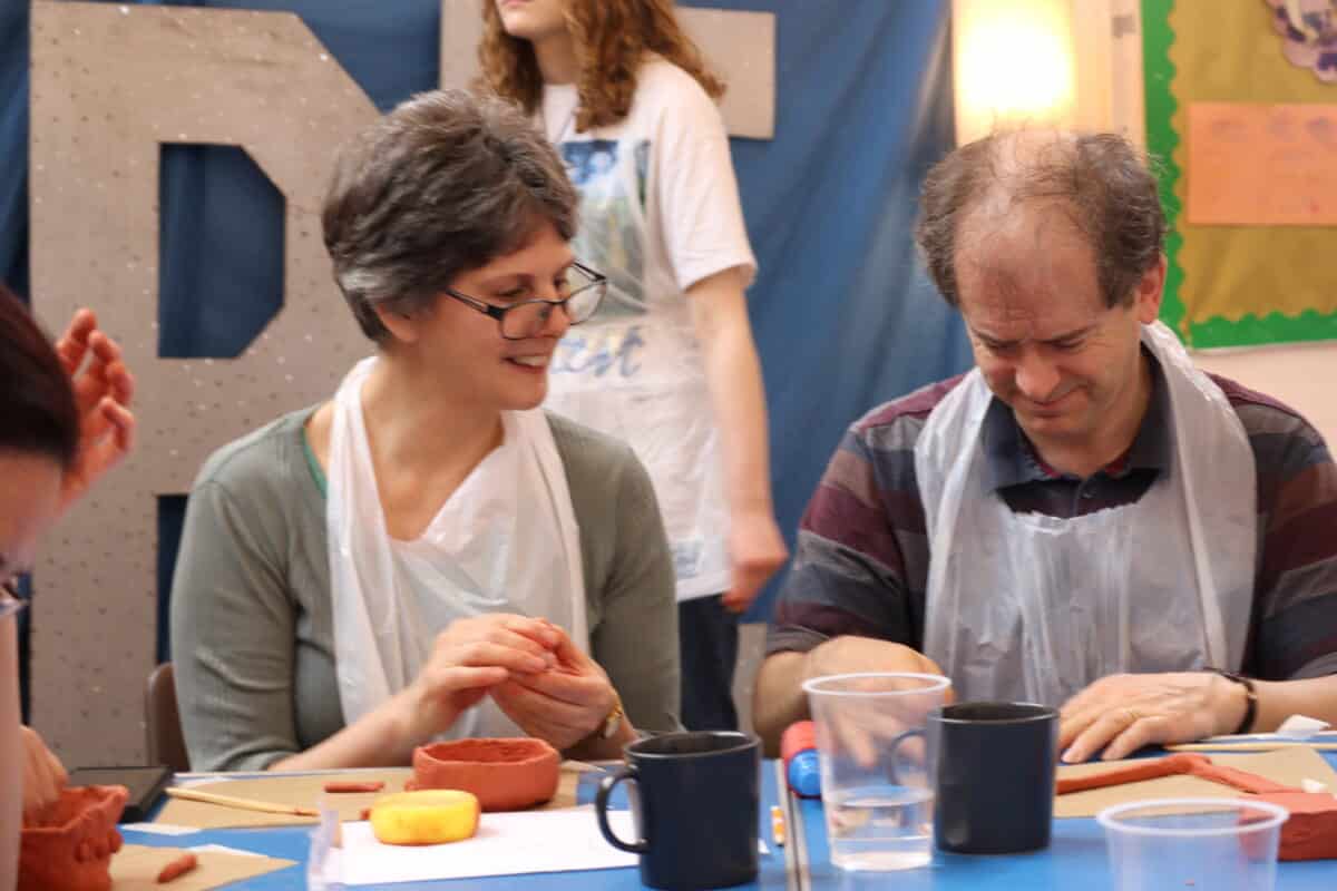 Two adults wearing aprons shaping clay