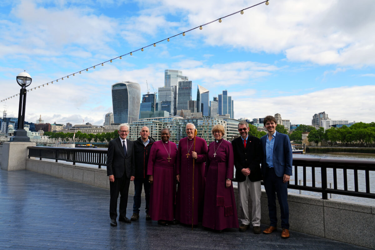 A group including Bishop Sarah standing on a walkway in front of the River Thames